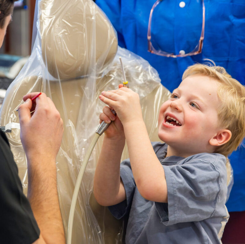 Young boy smiles while holding up dental suction device during Roseman's annual Give Kids a Smile event.