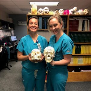 Dr. Kimberly Veltman and a classmate smile broadly as they show off a pair of skulls with surgical markings.